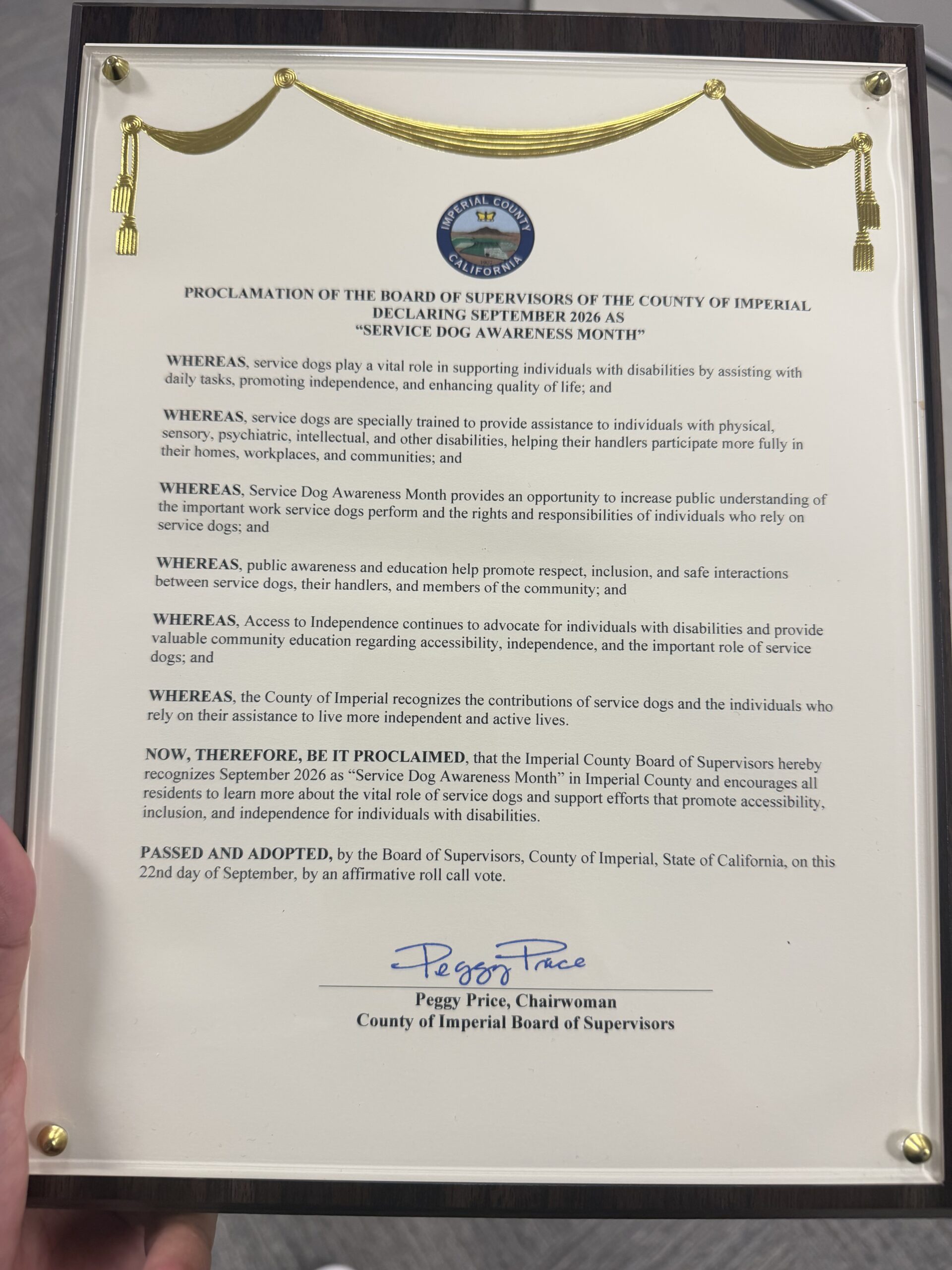 Framed proclamation plaque from the Imperial County Board of Supervisors declaring September 2026 Service Dog Awareness Month. The Imperial County seal sits beneath a gold drape, and the proclamation is signed by Board Chairwoman Peggy Price.